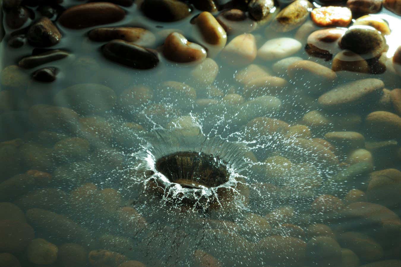 BG1BW6 A pebble dropping into a shallow stony pool.