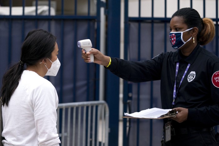 A volunteer checks the temperature of a poll worker at an early voting polling location for the 2020 presidential election at the Nationals Park baseball stadium in Washington, DC in October 2020