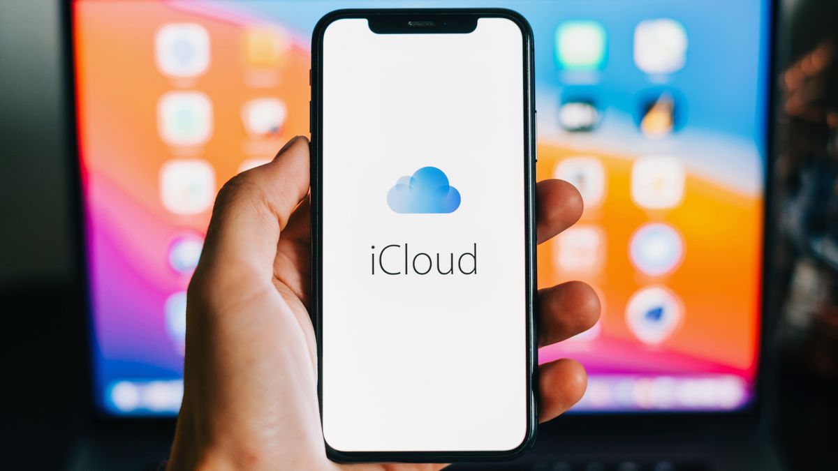 A hand holding an iPhone with the iCloud logo on screen.