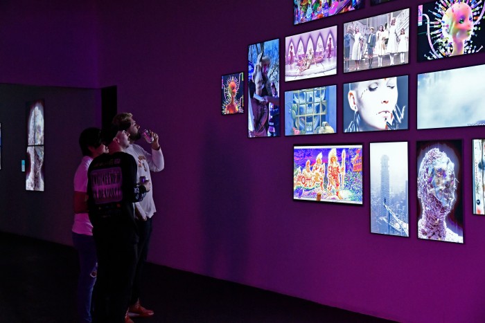 Three young men look at artworks mounted on a purple wallin a darkened room