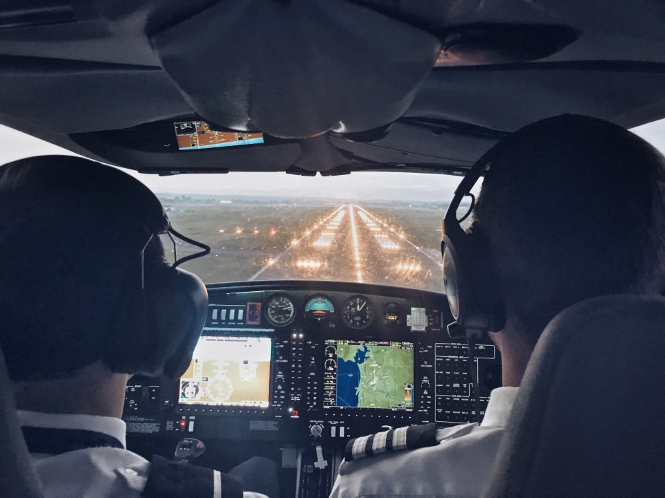 Two pilots in a cockpit landing at night with runway lights visible