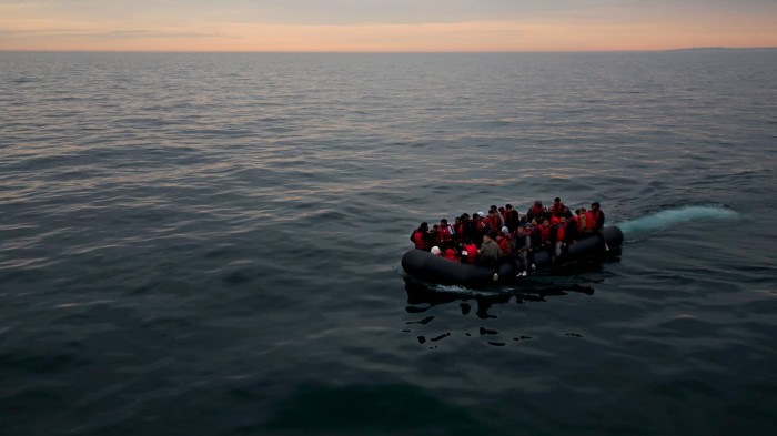 A crowded dingy carries passengers in life jackets across the ocean