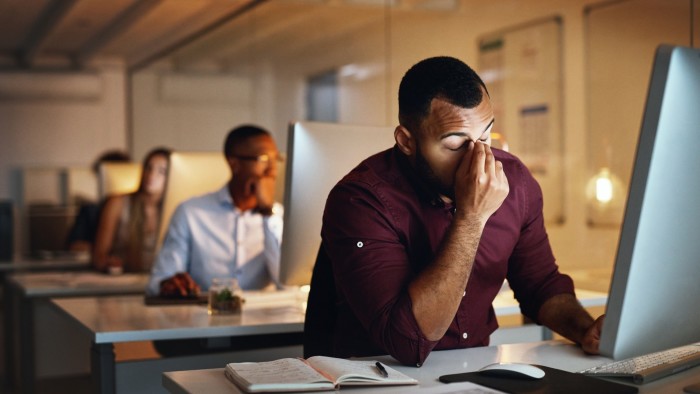 A man clasps his head in dismay while working late in an office