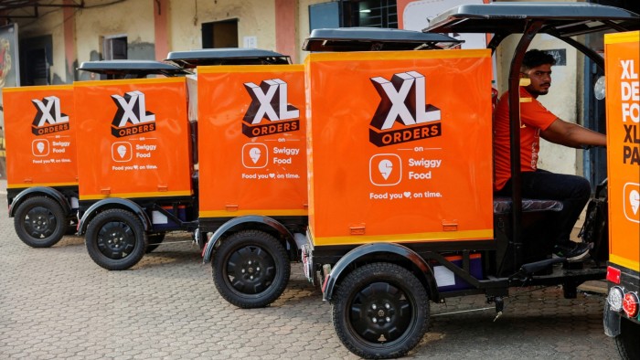 A line of Swiggy electric three-wheel delivery scooters