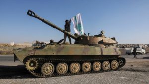 A Hayat Tahrir al Sham rebel fighter flies the group's flag atop a tank in Idlib province on 1 December. Pic: Reuters