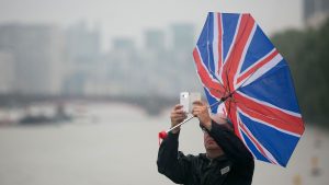 File photo dated 13/08/15 of a man's umbrella blowing inside out as he take a photo with his mobile phone in Westminster, London. Pic: PA