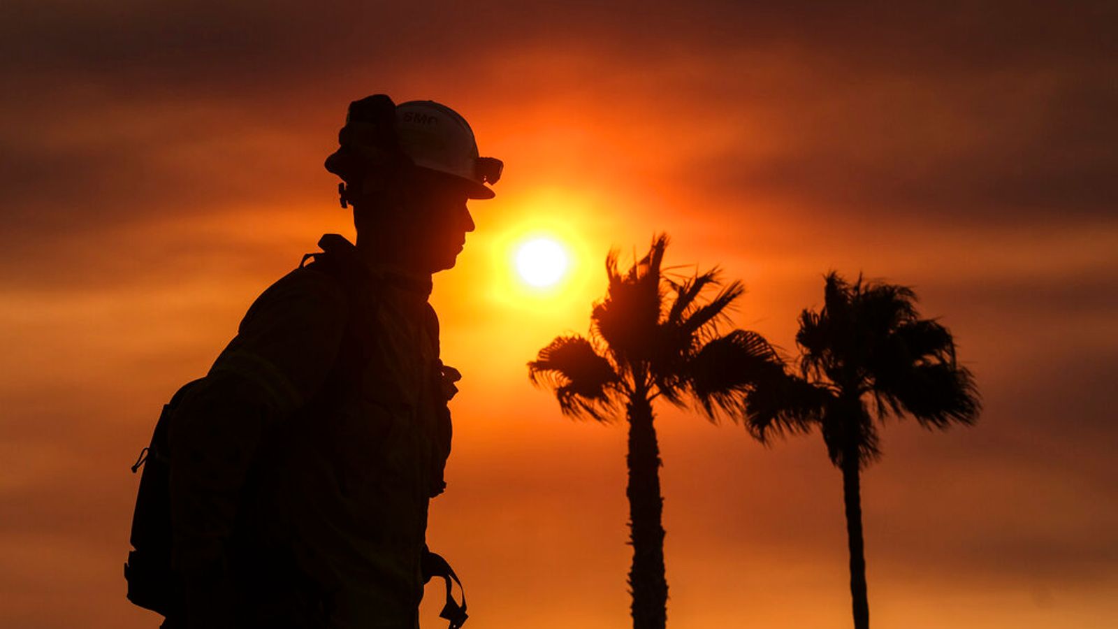 Wind blows the palm trees as a firefighter watches during sunset while a wildfire burns Tuesday, Sept. 6, 2022, near Hemet, Calif. (AP Photo/Ringo H.W. Chiu)