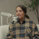 Jinger Duggar speaks into a mic while wearing a beige plaid shirt.