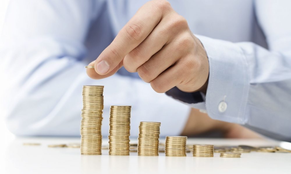 A hand adds another coin to a stack. (Shutterstock)