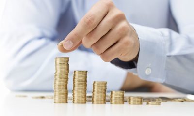 A hand adds another coin to a stack. (Shutterstock)