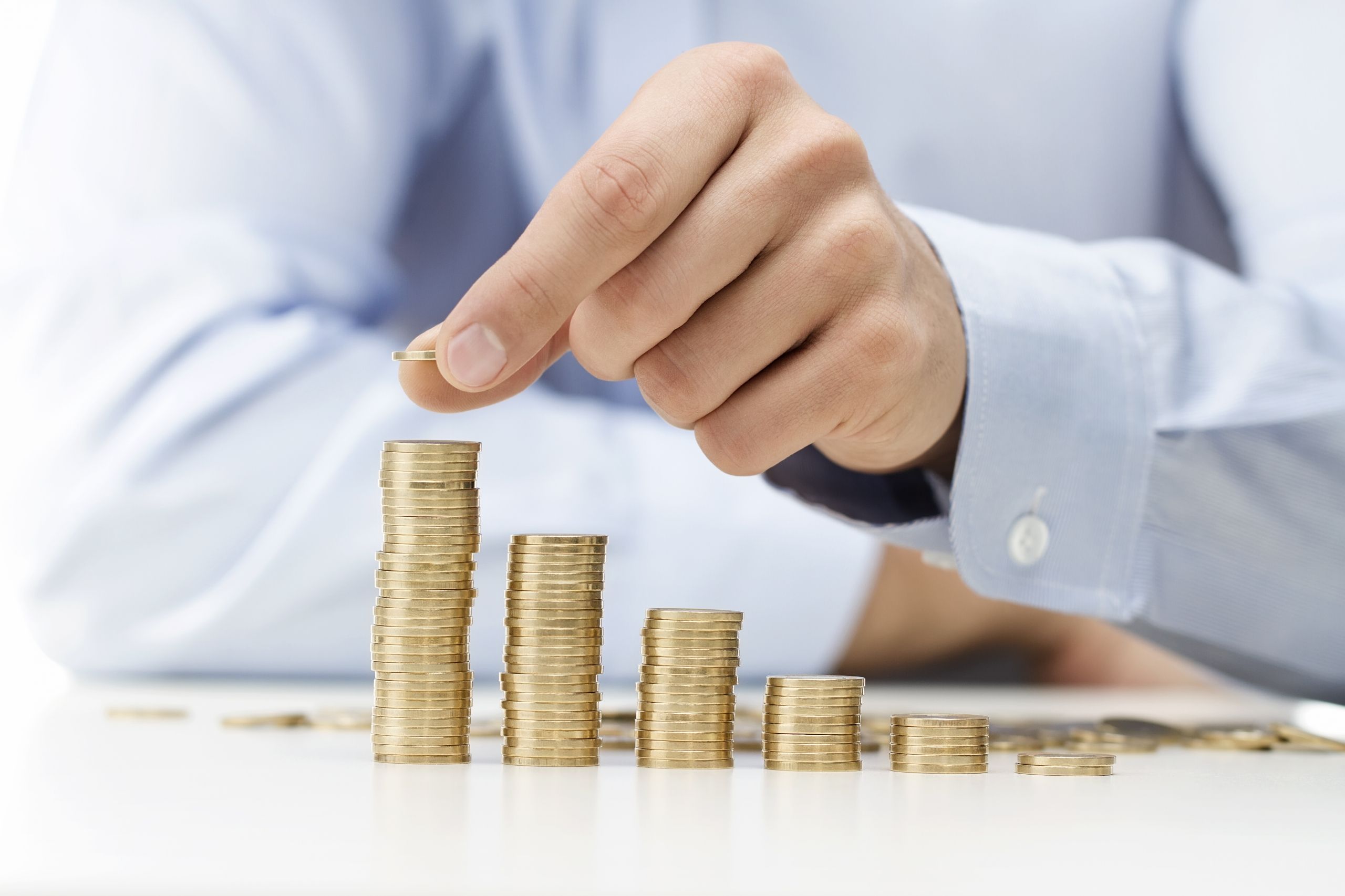 A hand adds another coin to a stack. (Shutterstock)