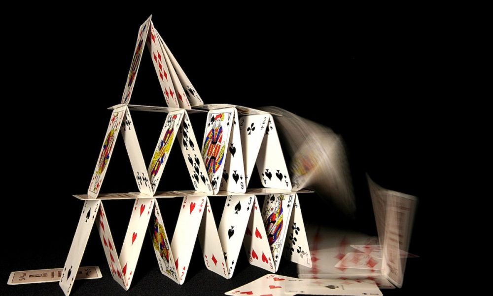 A house of cards collapsing on dark background