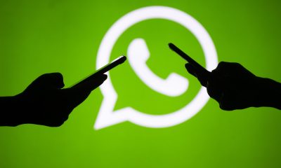 People hold mobile phones in front of the logo of WhatsApp application.