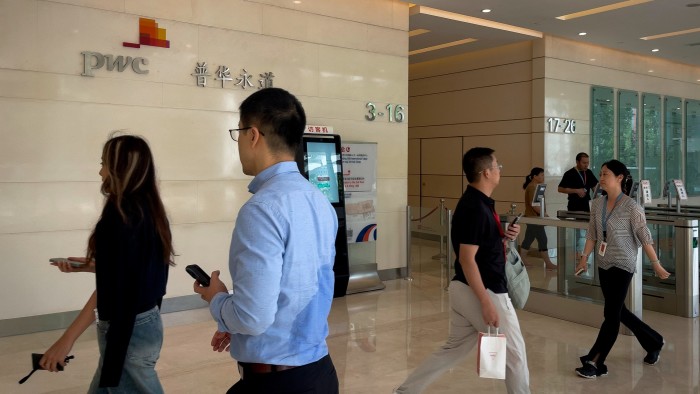 People walk through the lobby of PwC’s office in Beijing. The interior features a modern design with a polished floor and the PwC logo on the wall.