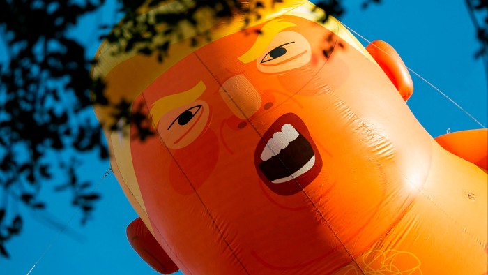 Looking up to a huge balloon depicting a face with an open mouth, flying in a blue sky
