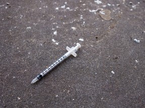 A used needle lying on pavement.