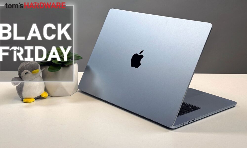 MacBook Air in sky blue on a white desk with a plant and a Black Friday sign.