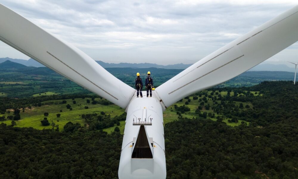 Two Electric engineer wearing Personal protective equipment working on top of wind turbine farm; climate tech investor survey