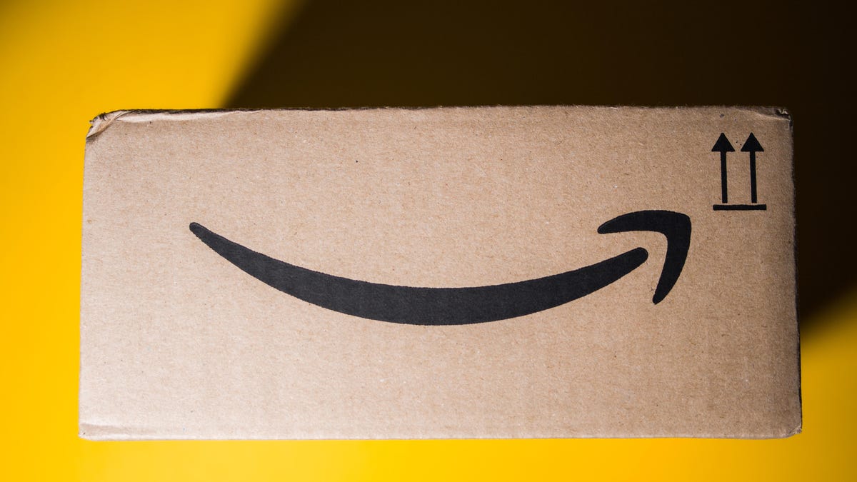 a side view of an old Amazon delivery box against a bright yellow background. the top left corner is covered in shade from the box&apos;s shadow