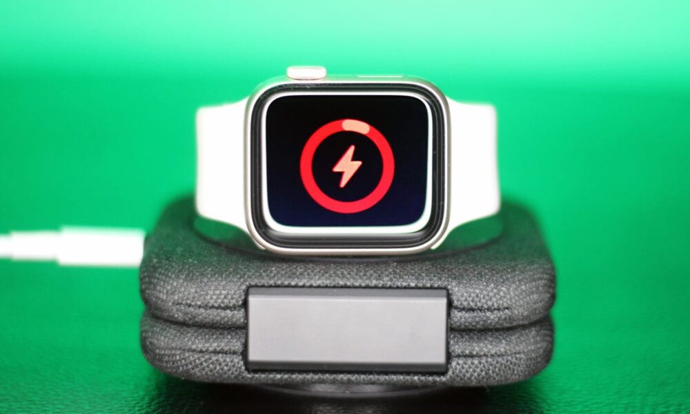 Apple Watch with white band charging on a dock, with a screen indicating low battery
