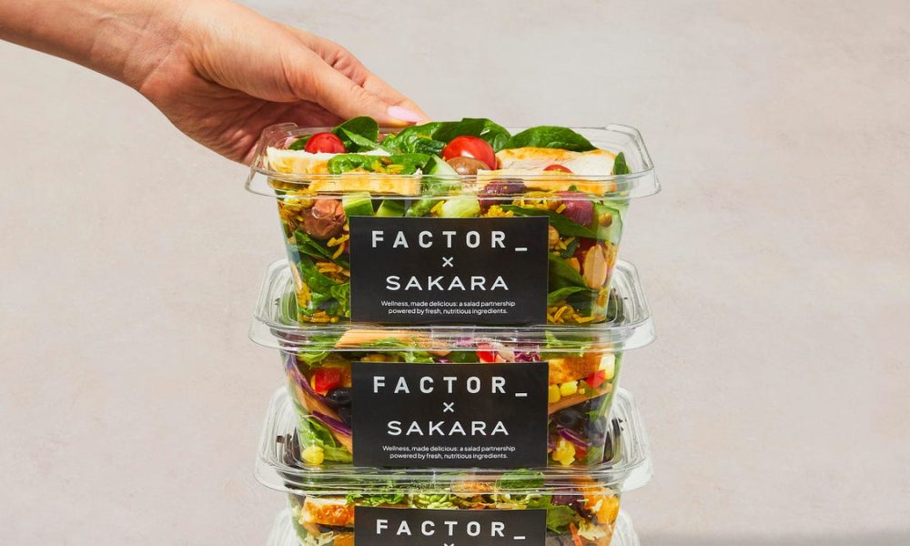 three salads in plastic containers with black labels stacked on top of each other