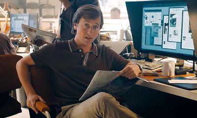 Jimmy Olsen sitting at his Daily Planet desk and holding a newspaper in 2025&#039;s Superman movie