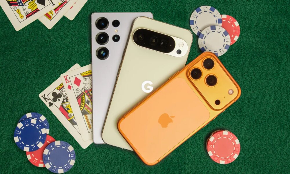 Three phones on a card table with cards and poker chips around them.