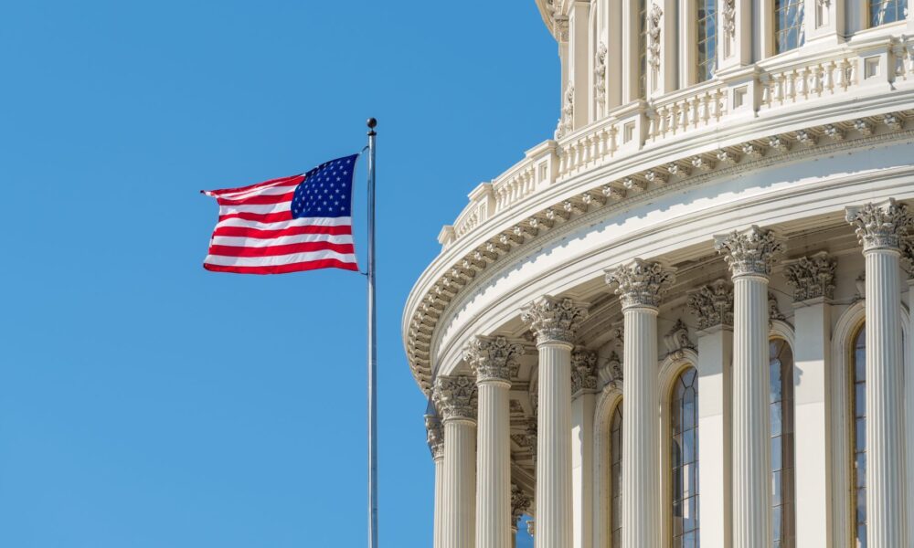 An American flag flying outside the US Capitol building against a blue sky