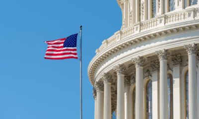 An American flag flying outside the US Capitol building against a blue sky