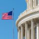 An American flag flying outside the US Capitol building against a blue sky