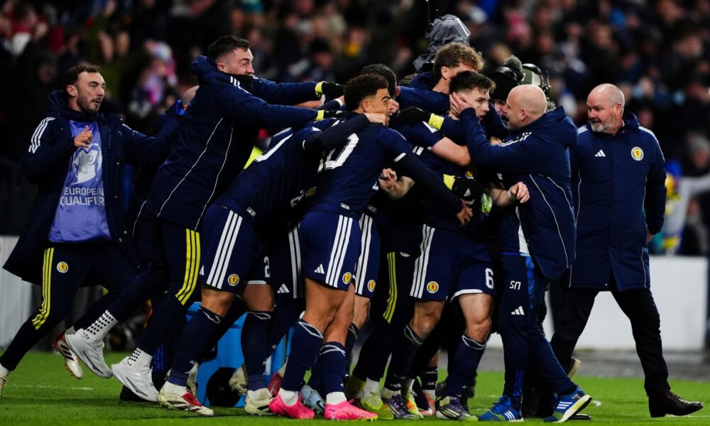 Kieran Tierney is mobbed by the Scotland bench after giving them a late 3-2 lead over Denmark
