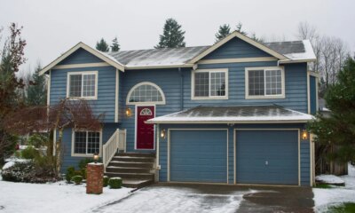 blue suburban-style house with snow covering the yard and driveway