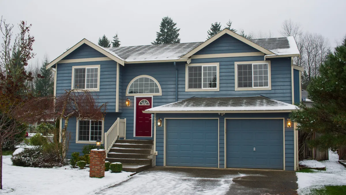 blue suburban-style house with snow covering the yard and driveway
