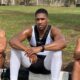 Anthony Joshua sits between Sina Ghami and Latif Ayodele as all wear training kit, with a grassy area behind the three men