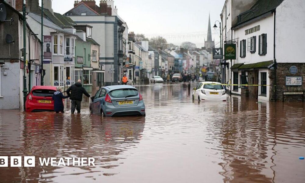 flooded street with cars submerged and a few people walking in the floodwater