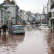 flooded street with cars submerged and a few people walking in the floodwater