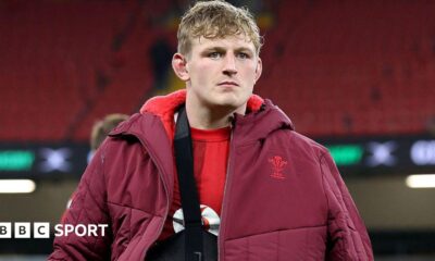 Jac Morgan wearing his arm in a sling under a red Wales-branded coat