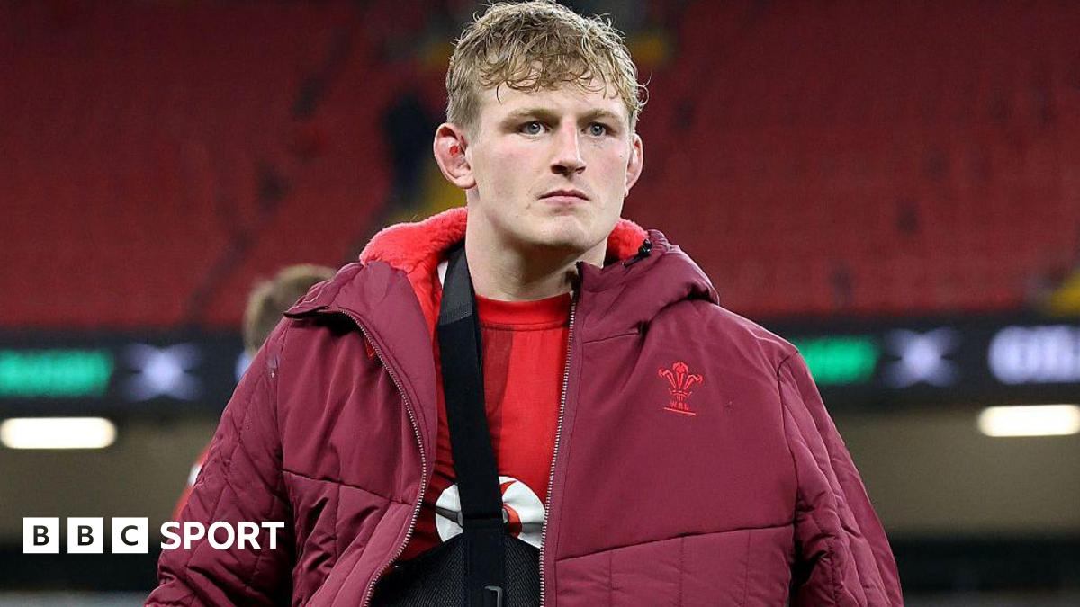 Jac Morgan wearing his arm in a sling under a red Wales-branded coat