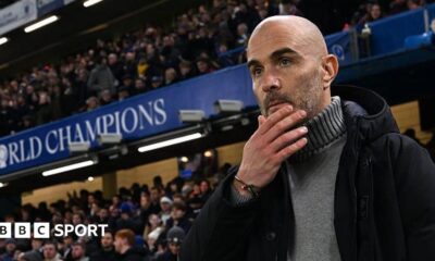 Enzo Maresca, manager of Chelsea, looks on prior to the Premier League match between Chelsea and Bournemouth at Stamford Bridge. He is wearing a grey jumper beneath a dark coat.