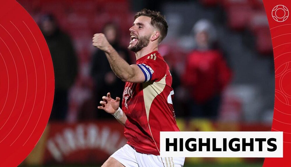 Luke Garbutt celebrates with fist in the air in red Salford City kit