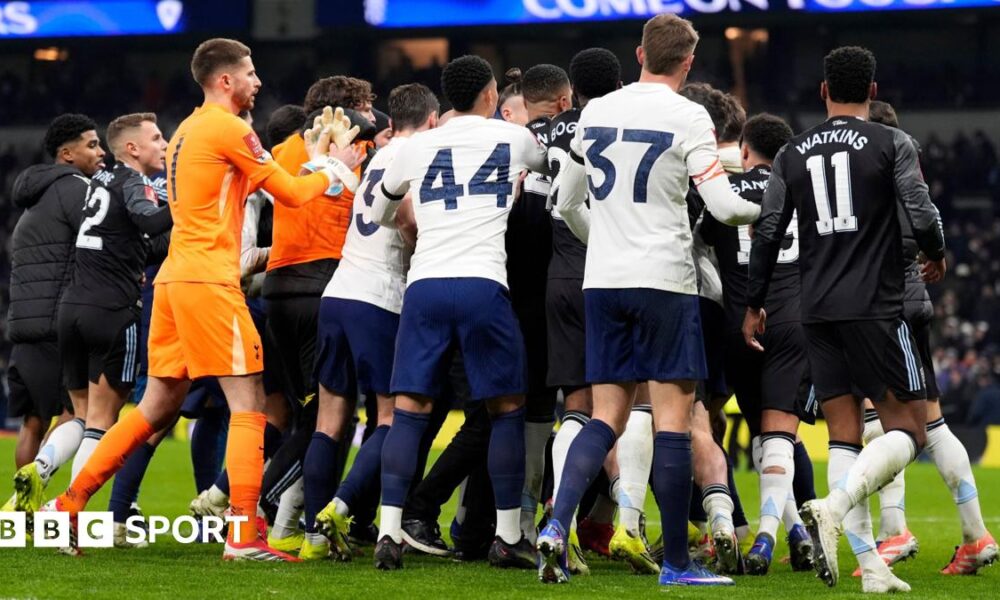 Tottenham Hotspur and Aston Villa players swarm in a melee after their FA Cup match, with the crowd in the distant background