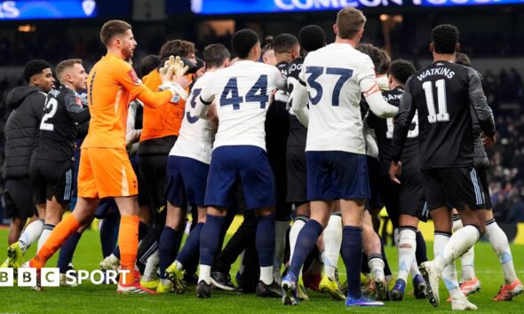 Tottenham Hotspur and Aston Villa players swarm in a melee after their FA Cup match, with the crowd in the distant background