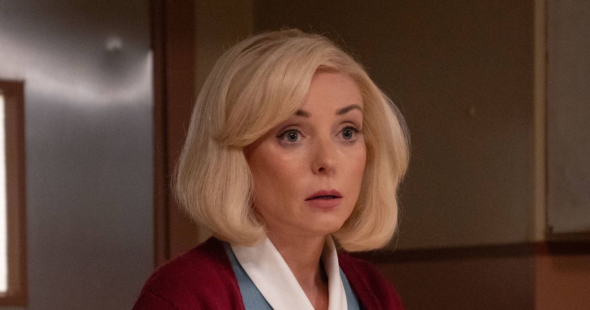 An individual in formal attire, accompanied by another person dressed in a blue gown, stands on a balcony, their gaze directed towards a body of water with boats and distant structures visible in the background.