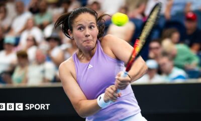 Daria Kasatkina, in a lilac tennis vest, plays a two-handed backhand shot as her eyes suggest intense focus