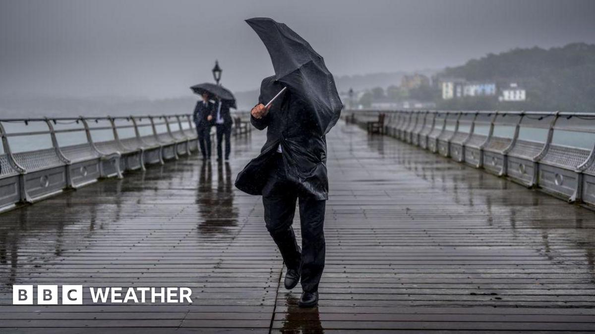 man holding an umbrella trying to shelter from heavy rain and breezy weather