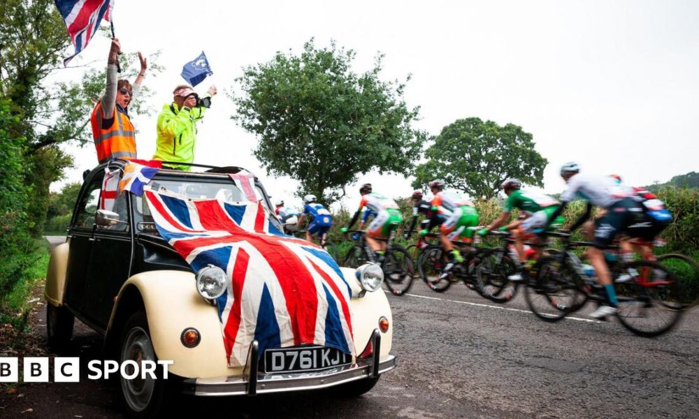 Fans wave flags in a car draped in a union jack as riders go past