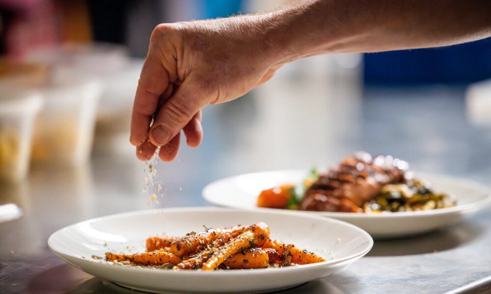 A hand puts the finishing touches on a plate of delicious carrots
