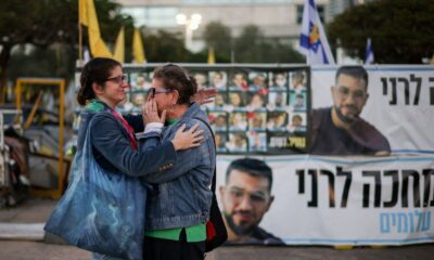 Israeli women hug in front of a banner with photos of former hostages, including Israeli police officer Ran Gvili. Pic: Reuters