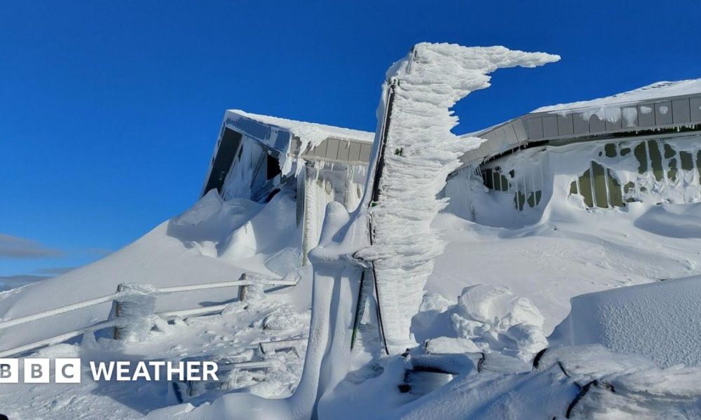 Bright blue skies are the back drop to a building with snow up the sides and on the ground and fence all around.