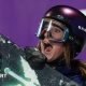 Mia Brookes shows an expression of delight, with her mouth wide open as she wears a protective dark-coloured helmet and ski goggles while carrying a snowboard